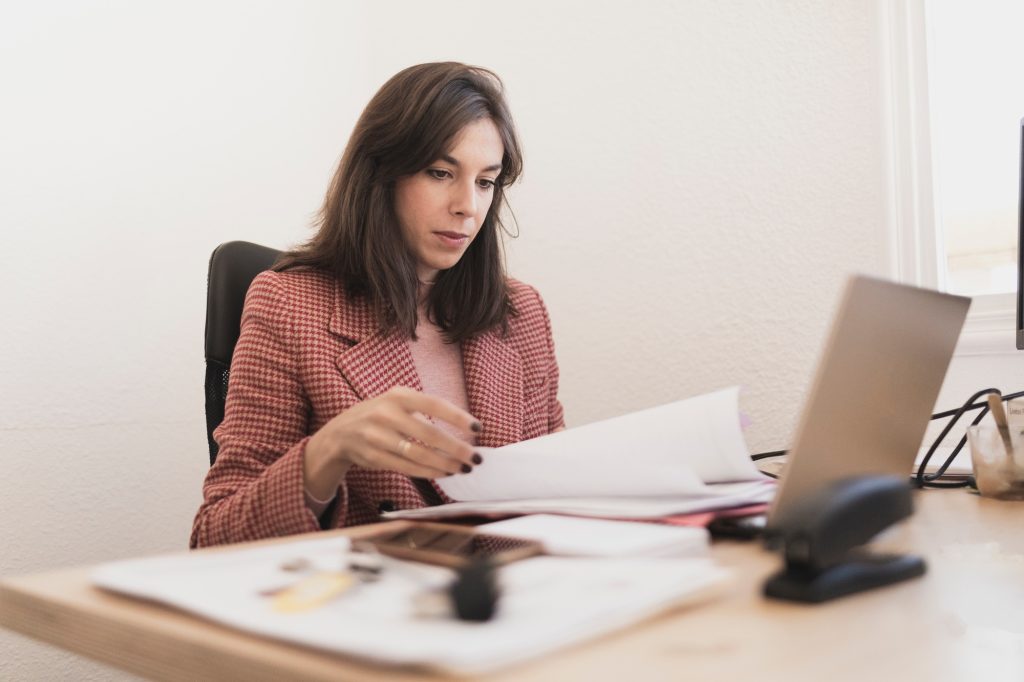 Serious woman with documents near laptop at workplace